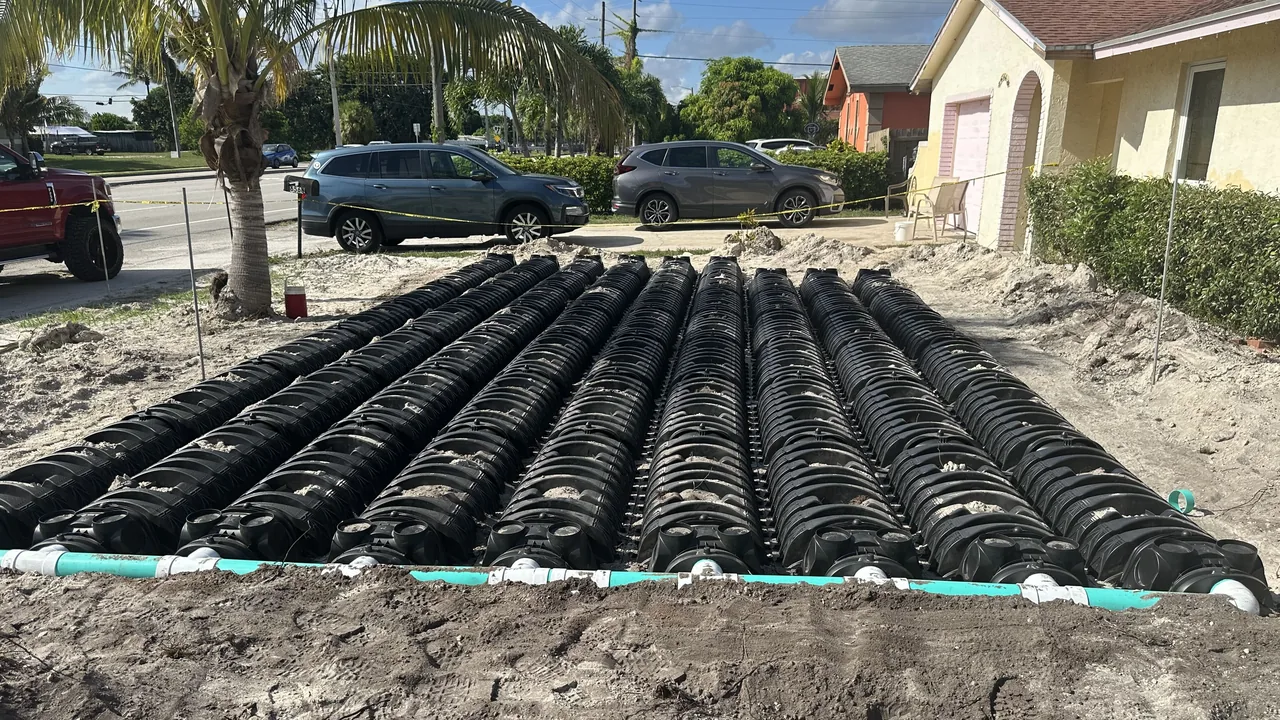 New drain field chambers lined up in a sandy front yard with a palm tree and parked cars, septic system installation