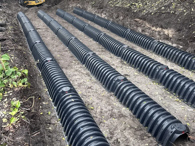 Black septic drain field chambers set in rows in a trench under trees, septic system installation