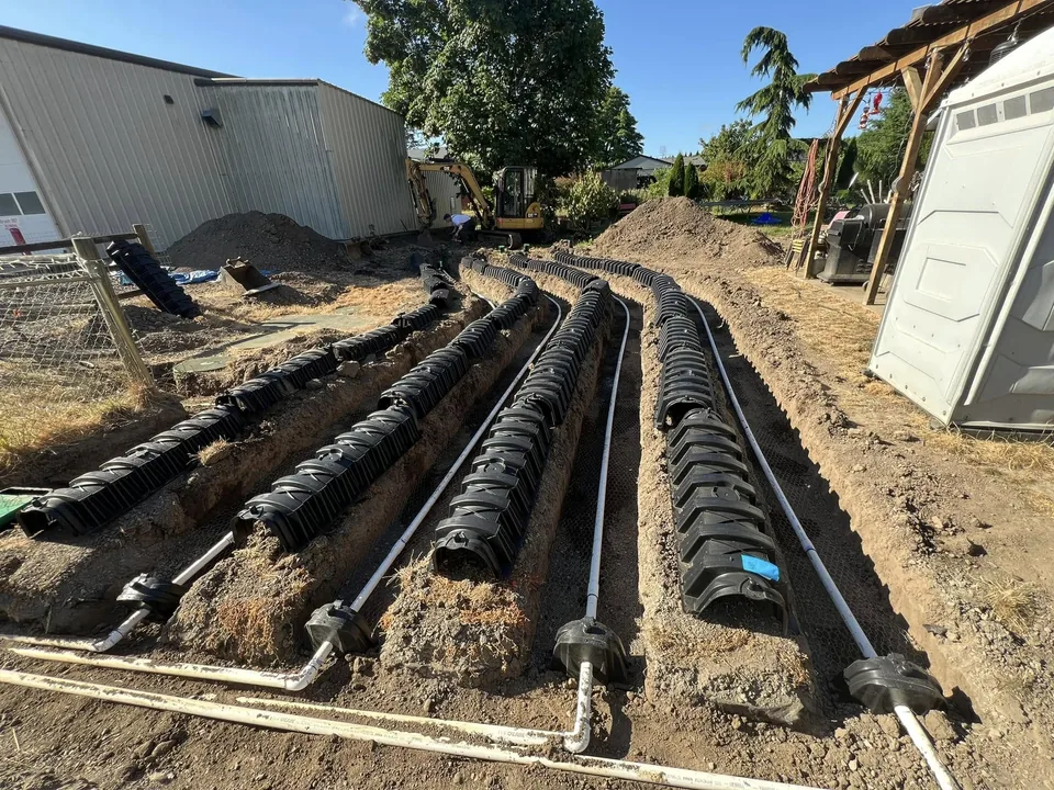 Drain field chambers and white pressure lines in open trenches with a mini excavator behind, drain field repair
