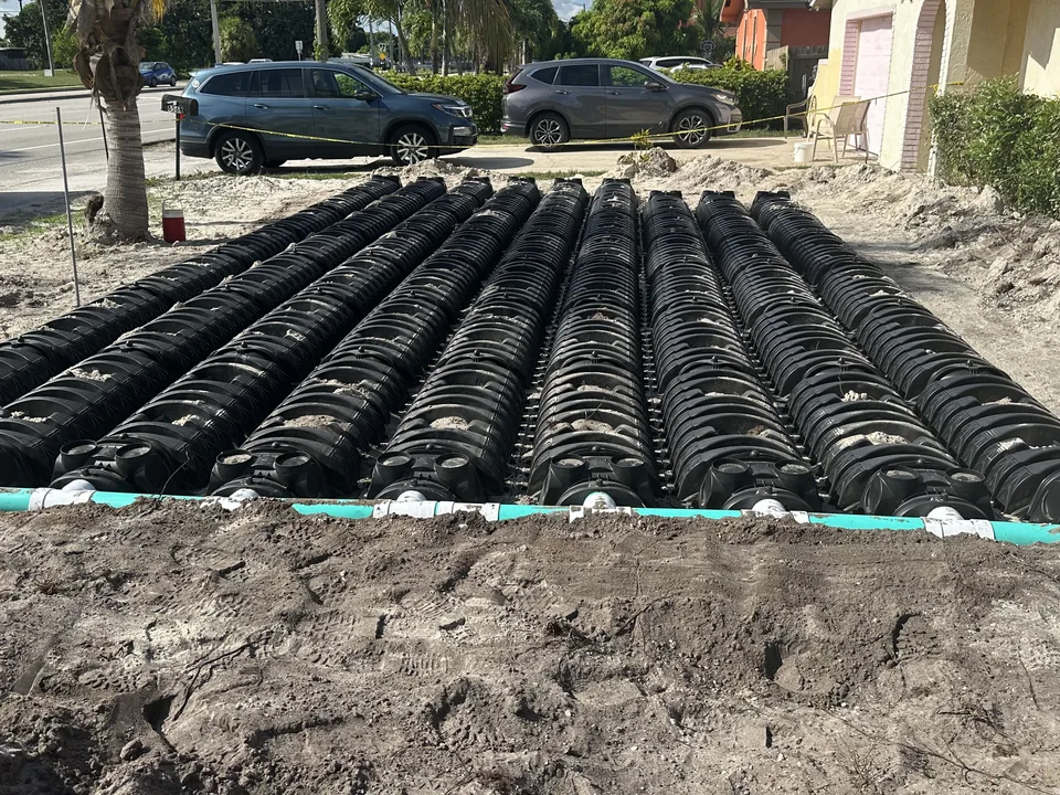 Rows of black drain field chambers fed by a green distribution pipe in a sandy yard, drain field repair