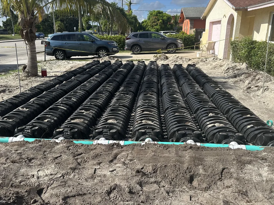 Close view of black drain field chambers and a green pipe in sandy soil, emergency septic service