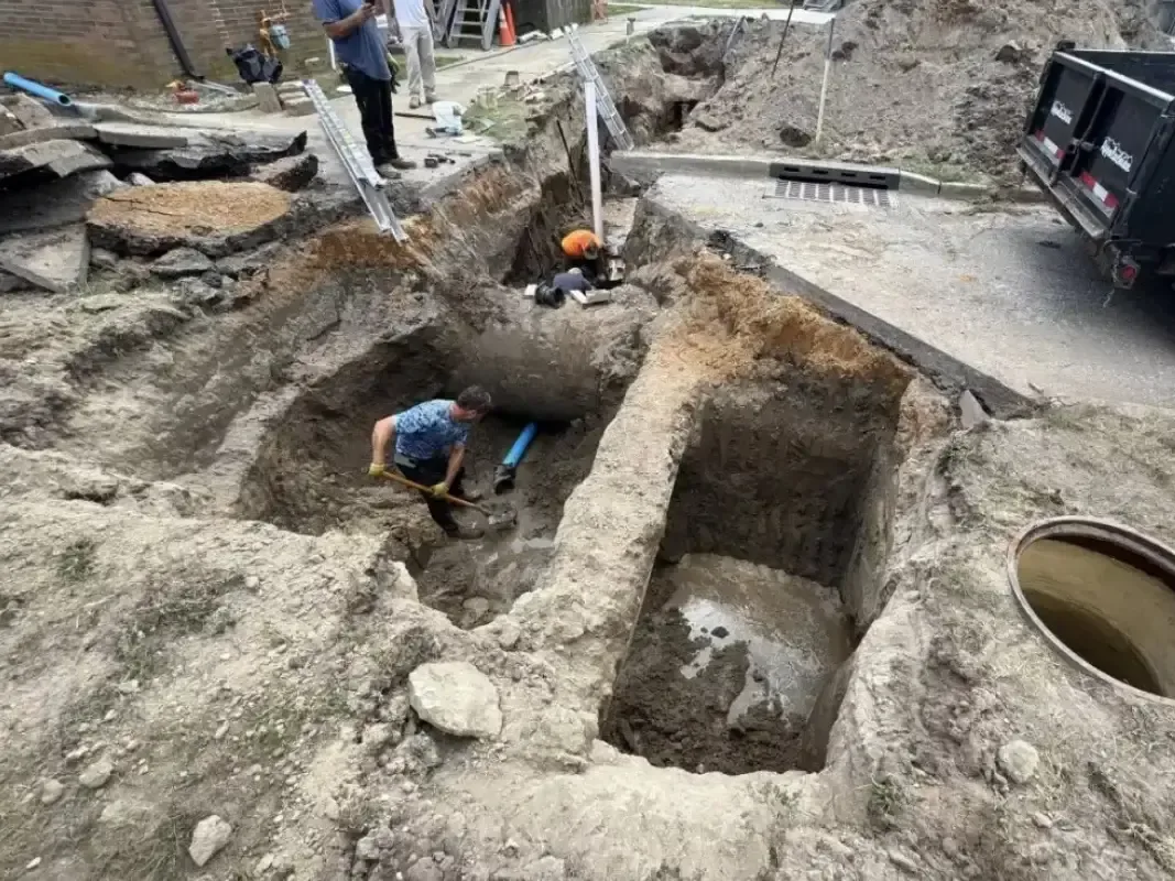 Deep excavation around a buried septic line with a worker digging in the pit, emergency septic service