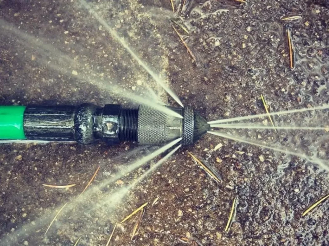 Close view of a jetter nozzle on a green hose spraying water jets across wet ground, hydro jetting