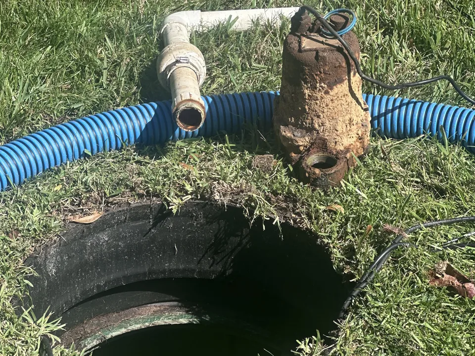 Old lift station pump pulled from its pump chamber beside the discharge pipe and a vacuum hose, lift station pump service