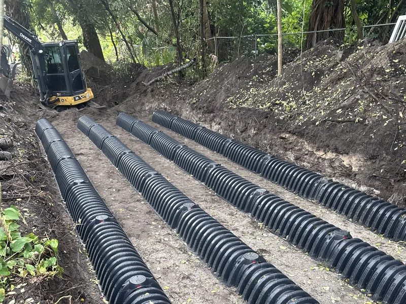 Mini excavator behind rows of drain field chambers set in a dug trench, septic system installation