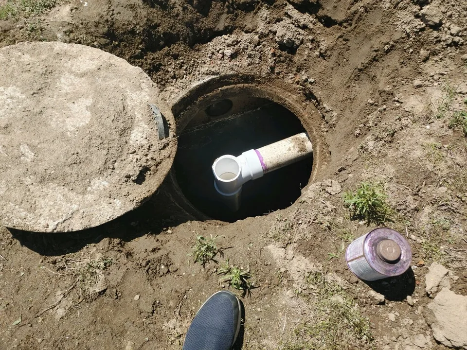 Round concrete lid lifted off a septic tank opening with a white outlet tee inside, septic tank filters