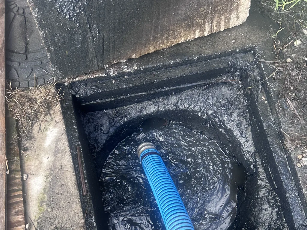 Open septic tank with its concrete lid lifted aside and a vacuum hose in the tank, septic tank inspection