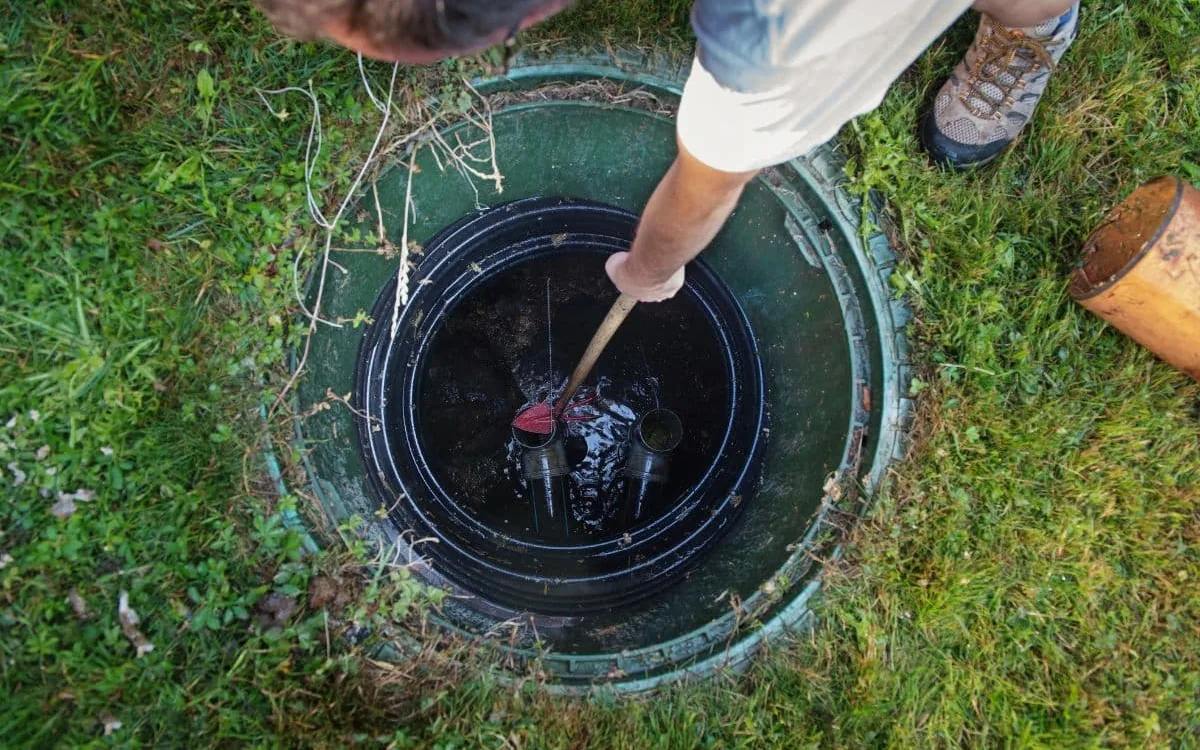 Looking down into an open green riser as a hand pushes a probe stick into the tank beside the tees, septic tank inspection
