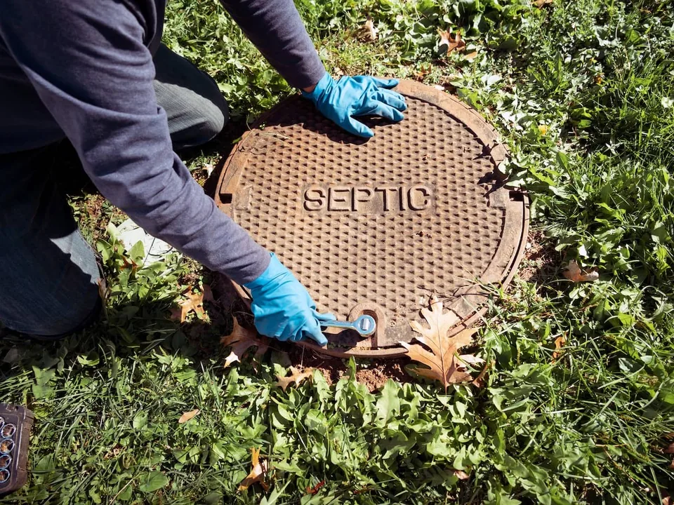 Gloved hands loosening the bolt on a cast iron septic tank lid with a wrench, septic tank inspection