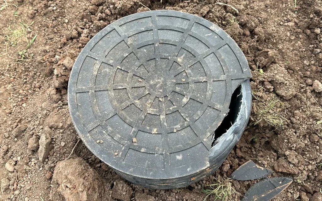 Cracked plastic septic tank lid and riser at grade with broken pieces beside it, septic tank lid replacement