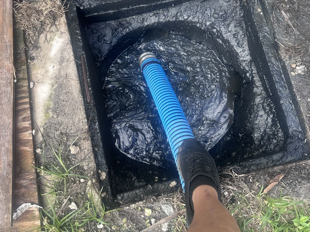 Close view of a vacuum hose drawing waste out of an open septic tank, septic tank pumping