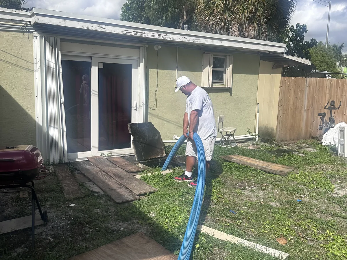Technician feeding a vacuum hose into an open septic tank behind a house, septic tank pumping