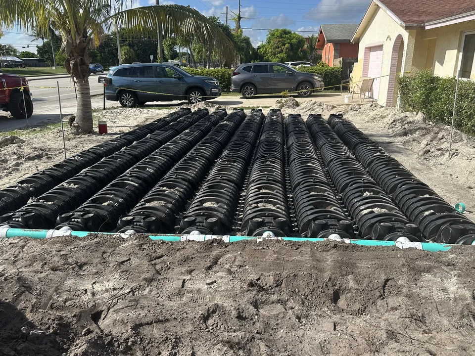 Black drain field chambers laid in rows across a sandy yard beside a house, septic tank repair