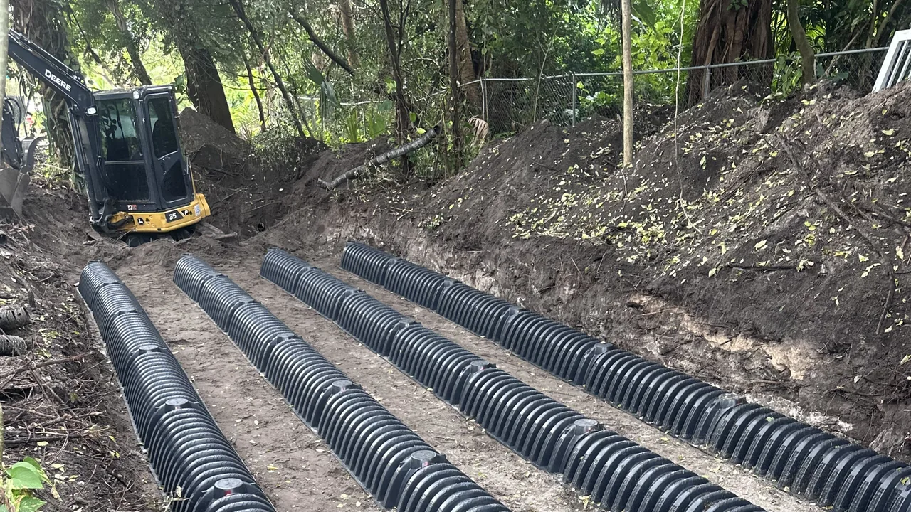 Rows of drain field chambers in a dug trench with a mini excavator behind, septic system installation